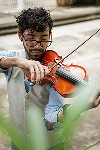 拉小提琴摄影照片_穿着背心的帅哥在户外拉小提琴。