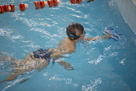 游泳池里戴着泳帽和泳镜的男孩。