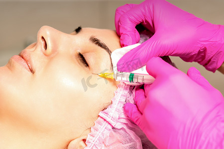 这位年轻的白人女性正在一家美容诊所接受面部注射，在眼睛上注射透明质酸。