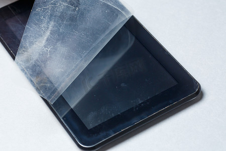 灰色背景上带有保护膜的黑色划痕平板电脑。