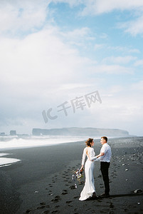 新娘和新郎站在冰岛的黑色维克海滩上