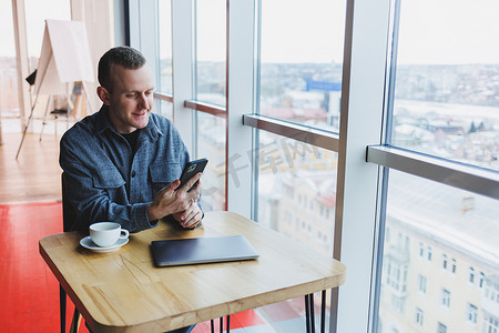 微笑的男经理坐在咖啡馆里使用手机小工具，通过在线应用程序订购送货服务，咖啡馆内免费 4g 无线网络，快乐的自由职业者在手机上发短信