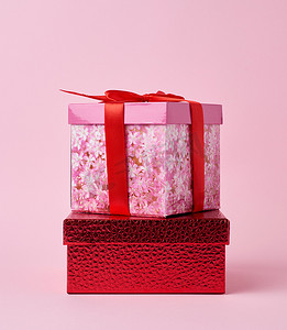 粉色背景活动摄影照片_粉色方形纸板盒，在粉色背景上系着红色蝴蝶结