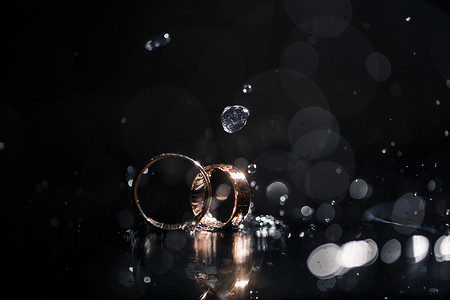 婚礼当天新婚夫妇的金结婚戒指，背景为黑色，水滴。