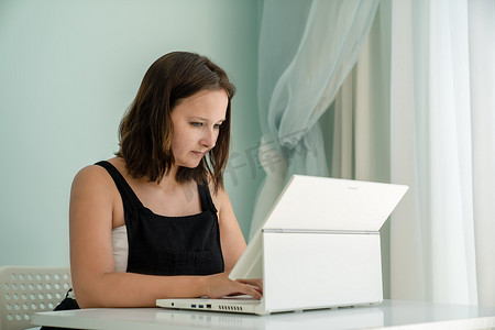 女孩正坐在家里桌子上的笔记本电脑变压器前。