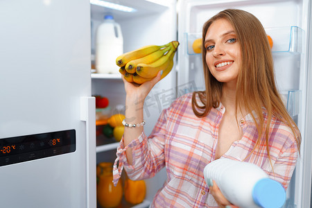 一位年轻金发女子从冰箱里拿食物的肖像
