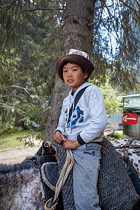 蒙古摄影照片_可爱、微笑的亚洲男孩骑马在山里骑行