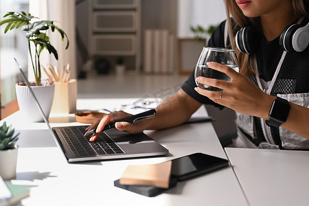 年轻女性自由职业者坐在明亮的家庭办公室里拿着一杯水，在笔记本电脑上打字的剪影