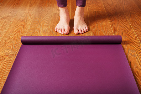 女孩的脚站在木地板上一张展开的瑜伽垫前。