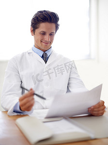这些结果很有希望……一位微笑的年轻医生坐在办公桌前处理文书工作。