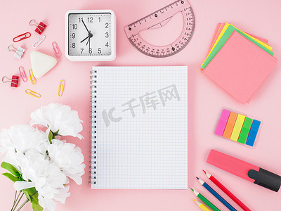 粉色办公桌面的顶视图，笔记本放在笼子里，鲜花，桌子上的学校用品，文字空间。