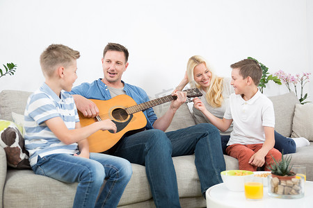 快乐的白人家庭在舒适的现代家中微笑、弹吉他和唱歌
