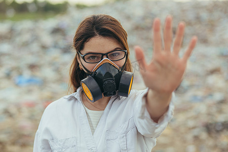 垃圾填埋场一名穿着防护呼吸服的妇女，双手举在前面，试图阻止地球的污染，并用手打出停车标志