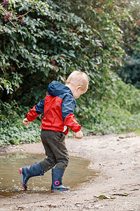 穿着红色防水外套的孩子在雨中在水坑里跳跃。