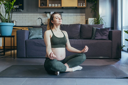一名孕妇在家里以莲花的姿势冥想和练习瑜伽