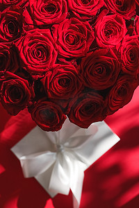 惊喜礼盒摄影照片_豪华假日丝绸礼盒和红色背景的玫瑰花束、浪漫惊喜和鲜花作为生日或情人节礼物