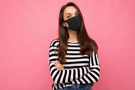 戴口罩的熊猫摄影照片_年轻美丽的黑发女性脸上戴着可重复使用的病毒防护面具，以对抗在粉红色背景墙上隔离的冠状病毒的照片，有可用的文字空间
