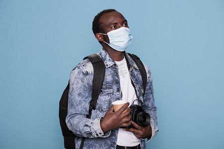 摄影爱好者戴着病毒防护面罩，同时携带数码单反相机和背包进行度假旅行