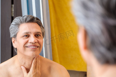 一个头发灰白的成年男子在剃须后微笑着照镜子