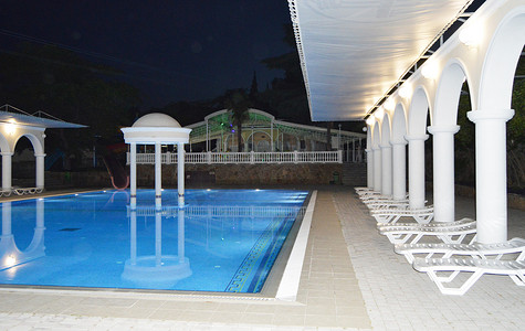 豪华泳池的夜景，配有柱子和拱门，倒映在水中