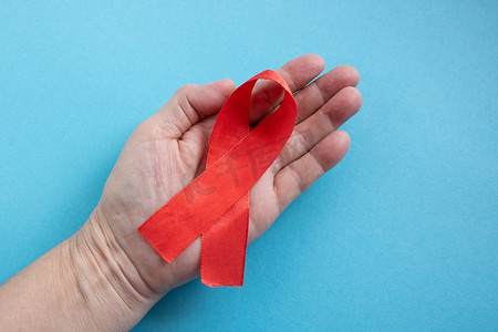 一只手握着蓝色背景上的红丝带 — 世界艾滋病日、捐赠者日、血友病日的概念