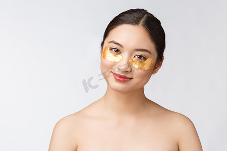 护肤品金色摄影照片_亚洲美女少女在眼睛下方用金色眼罩贴片护理皮肤