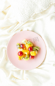 水果平铺摄影照片_丝绸上的多汁水果沙拉，平铺-健康的生活方式和床上早餐概念