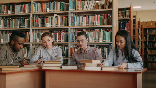 考试准备摄影照片_多民族学生坐在大学图书馆的桌子旁聊天和准备考试