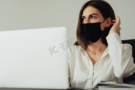 坐在办公室的女员工肖像、戴着防护面具、在笔记本电脑上工作的年轻女性