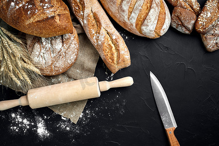 小棍黑板摄影照片_法式长棍面包、烤面包、面粉和小麦穗组合物的顶视图，深色背景上撒有小麦粉