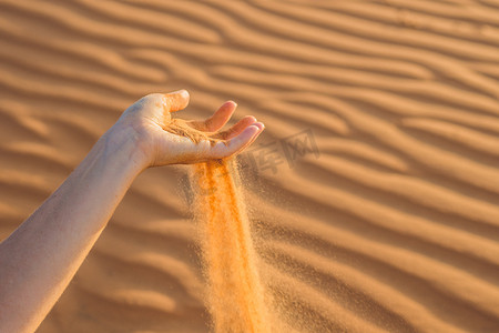手指天空摄影照片_沙漠中，沙子从女人的手指间滑落
