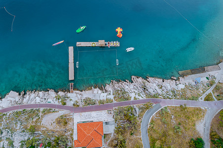 蓝色亚得里亚海的顶视图，海中的双体船，靠近大海的石头海滩，有一条步行道。
