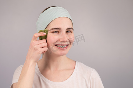 戴牙套摄影照片_一位戴着牙套的微笑女士用水粉按摩器做家庭护理的特写肖像。