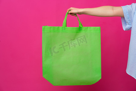粉色背景下女手拿着生态或可重复使用的购物袋
