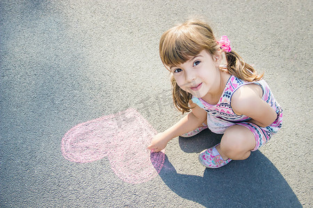 涂沥青摄影照片_孩子在沥青心上涂粉笔。