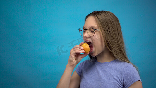 牙齿上戴着牙套的少女在蓝色背景下吃杏子。