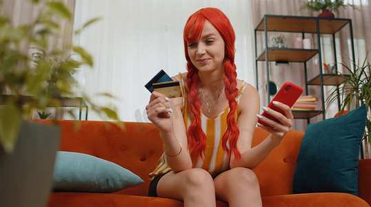 女人坐在沙发上使用信用卡和智能手机，同时在网上购物转账