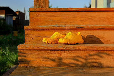 夏日后院旧橙色楼梯上的黄色橡胶泥泞工作鞋，日落时分，乡村和乡村正宗的心情
