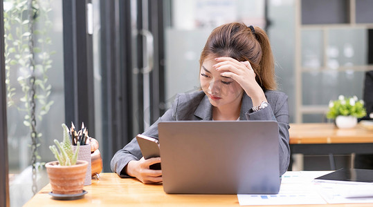 严肃的年轻亚裔女商人在她的办公桌前处理智能手机问题或收到老板的投诉电子邮件。