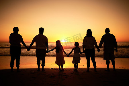 大家庭摄影照片_大家庭剪影在海滩上与海浪，日落在地平线上，手牵手发展健康、支持和爱。