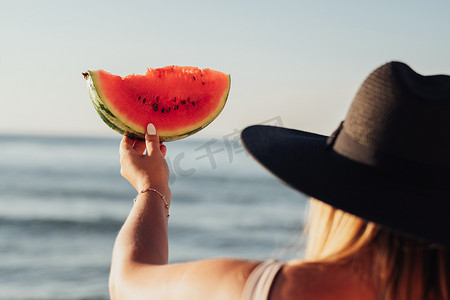 女人手里拿着一块西瓜对着大海的后视图，夏季时间概念