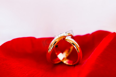 金色婚礼装饰摄影照片_红色玫瑰花瓣上的金色结婚戒指。