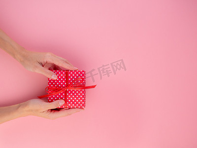 礼盒蝴蝶结摄影照片_女人拿着红色礼盒里的礼物，礼盒里有蝴蝶结、粉色背景、顶视图、空白的文字空间