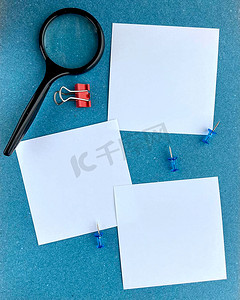 通知蓝色背景摄影照片_蓝色背景空白便条纸提醒或带有放大镜按钮和回形针的待办事项列表纸上的明信片模型。