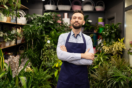 一位成功的男性花艺师站在他的店里，站在盆栽和花束之间，脸上挂着微笑。