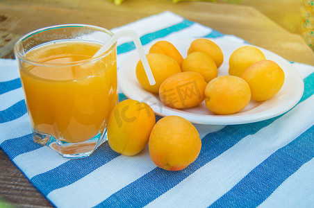 阳光明媚的户外，夏日饮料和水果鲜杏汁装在玻璃杯中，餐巾上放着吸管和成熟的杏子