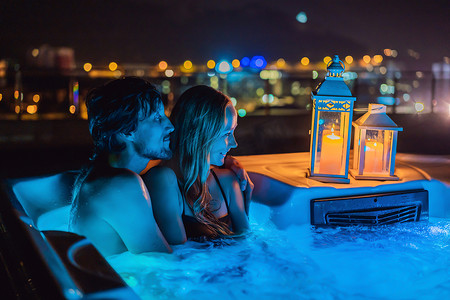 年轻无忧无虑的快乐微笑夫妇在热水浴缸中放松的肖像，在夜间绿色大山的背景下享受快乐的旅行时刻假期生活