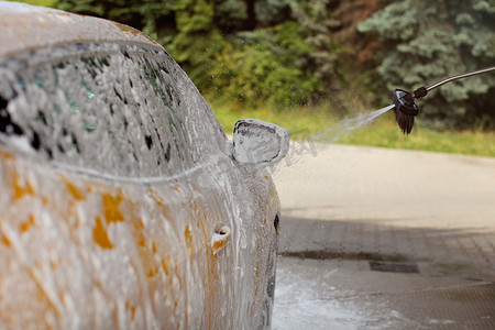 黄色汽车的侧镜和侧镜在自助洗车中清洗，泡沫和洗发水喷洒，滴在空气中。