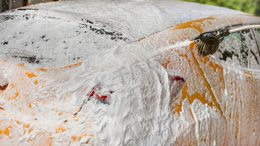 黄色汽车完全覆盖着洗发水和泡沫，更多喷涂，在自助洗车场。