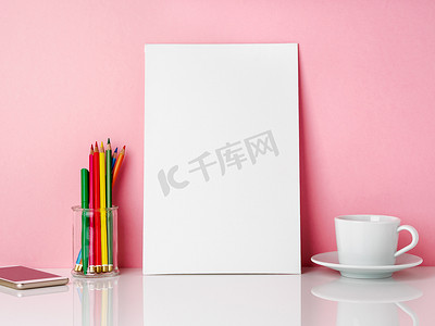 空白的白色框架和罐子里的蜡笔，白色桌子上的一杯咖啡和茶，靠在粉红色的墙上，有复制空间